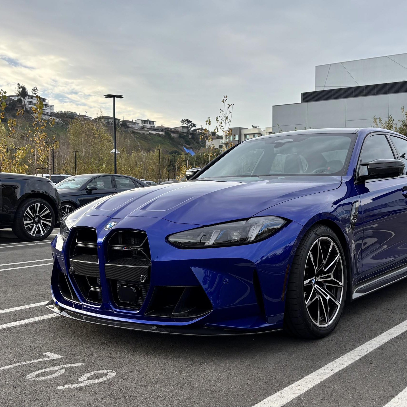 A blue BMW G8X M3/M4 with a carbon fiber front lip installed on the front bumper.