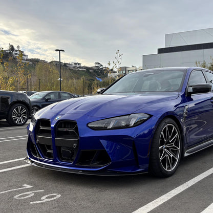 A blue BMW G8X M3/M4 with a carbon fiber front lip installed on the front bumper.